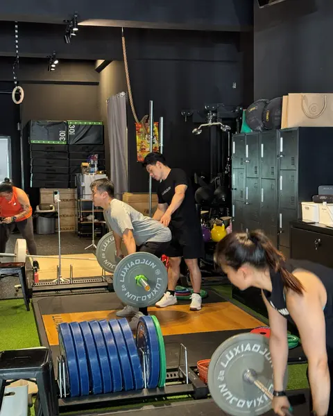 A lifter pulling a barbell from the platform while others train behind her.