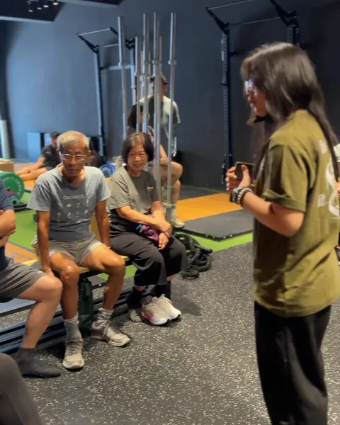 A coach leading a senior class while members rest on a bench between sets.