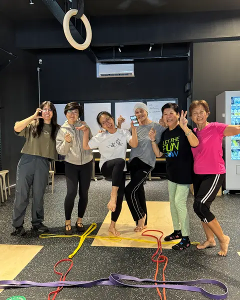 Six older members laughing together at the end of a senior class, resistance bands on the mats around them.