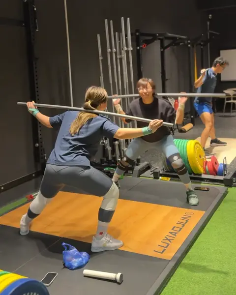 A member catching a barbell overhead at the bottom of a squat on a wooden platform.